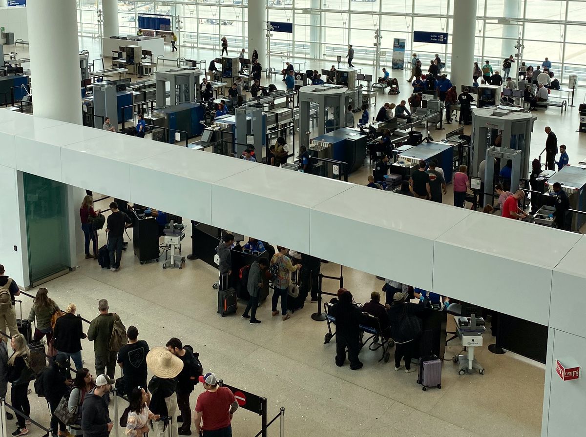Calm security checkpoint with stainless steel tables, stacked gray bins and a walk-through scanner in warm window light